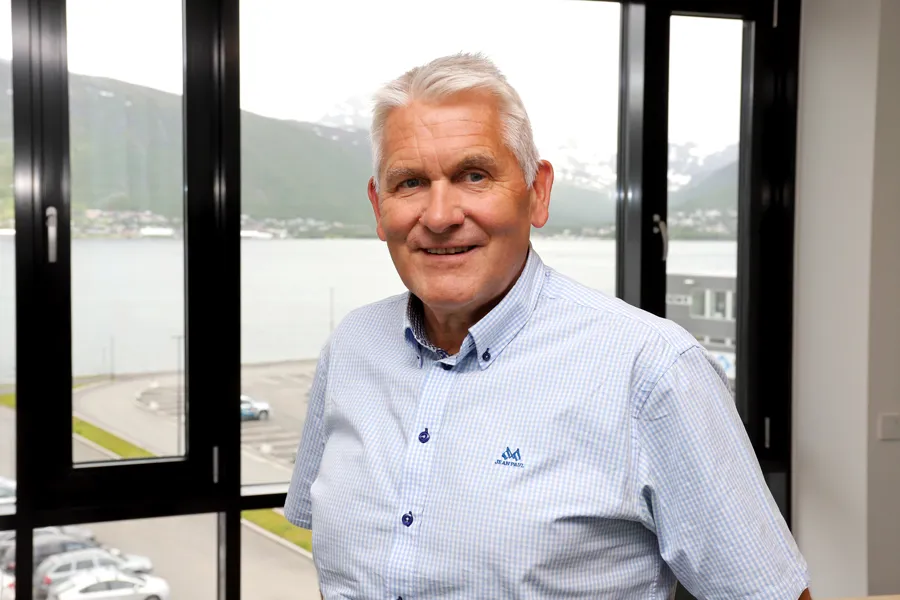 Oddbjørn Schei står foran vinduet på kontoret sitt i Tromsø