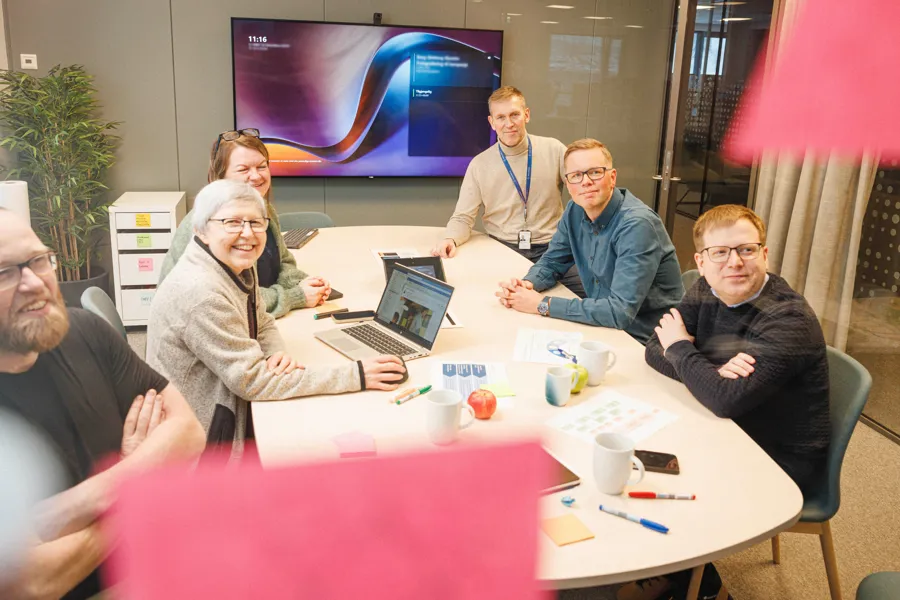 Flere mennesker sitter rundt et møteromsbord og smiler