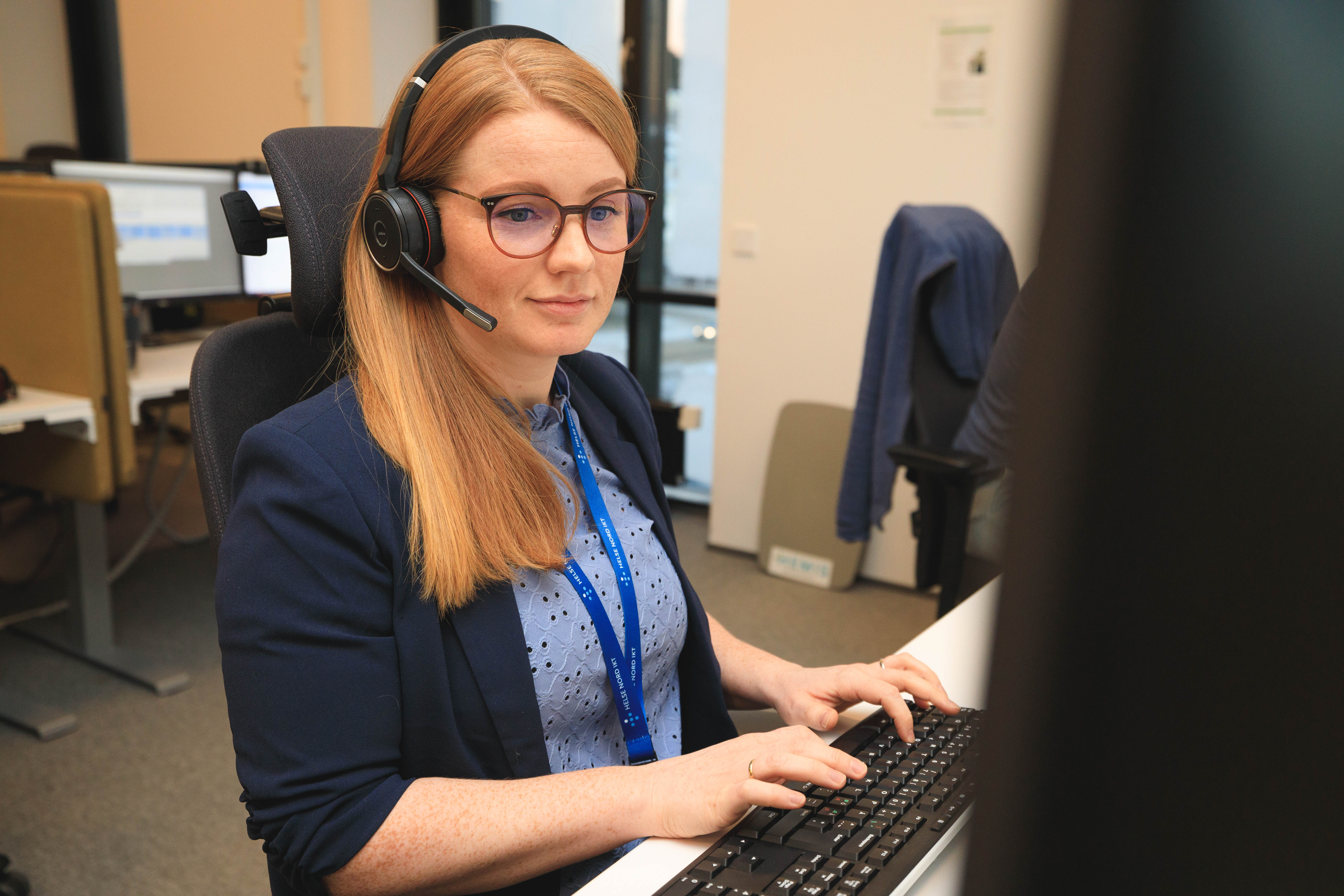 En kvinne som har på seg hodetelefoner og sitter ved en datamaskin