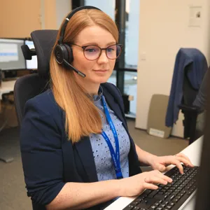 En kvinne som har på seg hodetelefoner og sitter ved en datamaskin