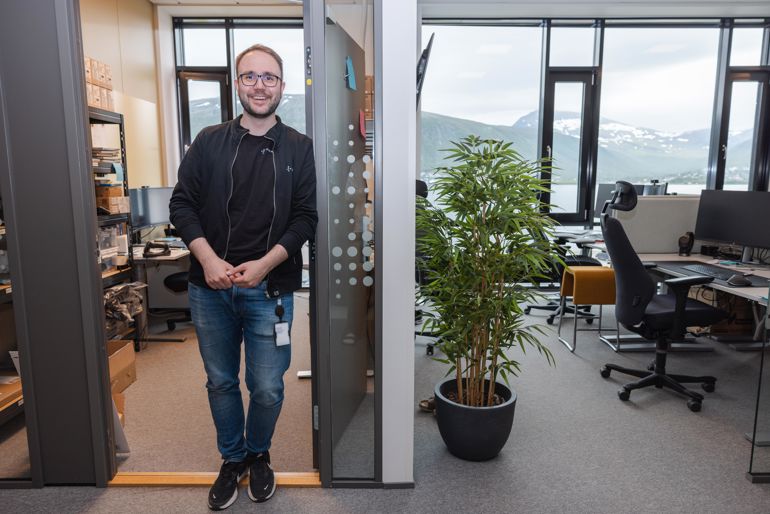 En person står i en døråpning og smiler i et kontorlokale.