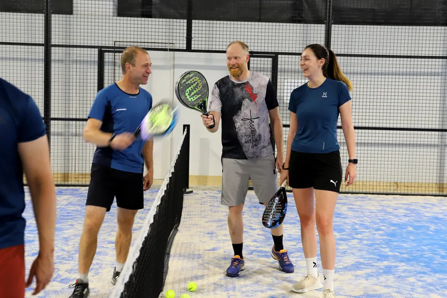 fire spreke og glade kolleger snakker med hverandre over nettet etter en runde padel