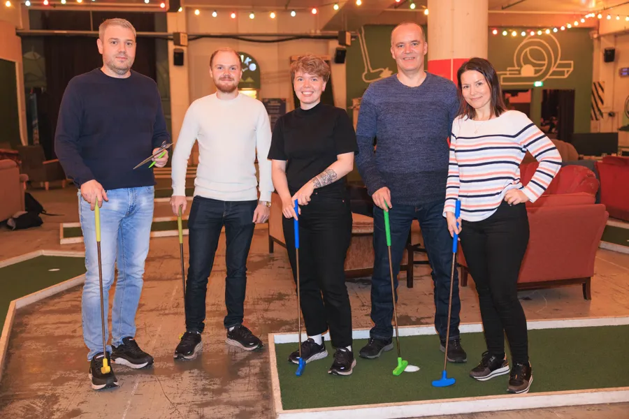 Fem mennesker står på en minigolfbane med køller og smiler.